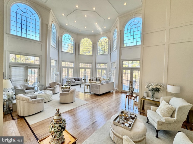 living room featuring crown molding, french doors, a towering ceiling, and light hardwood / wood-style flooring