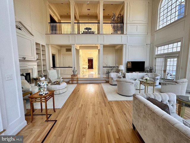 living room with a high ceiling, light wood-type flooring, built in shelves, and decorative columns