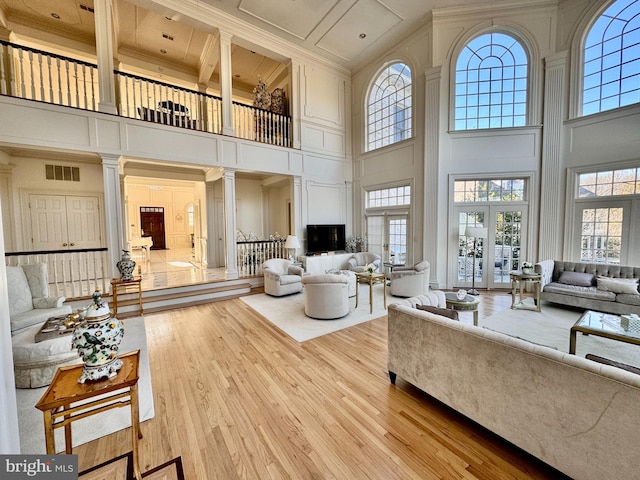 living room with ornate columns, a towering ceiling, light hardwood / wood-style floors, and a wealth of natural light