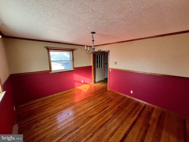 empty room featuring a textured ceiling, ornamental molding, a chandelier, and wood-type flooring