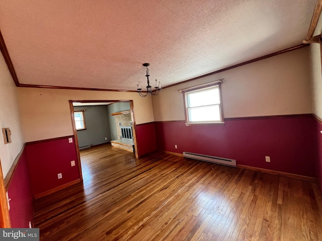 spare room featuring a brick fireplace, a textured ceiling, a baseboard radiator, dark wood-type flooring, and an inviting chandelier