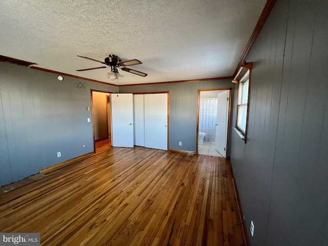 unfurnished bedroom featuring ceiling fan, a textured ceiling, ensuite bath, hardwood / wood-style flooring, and ornamental molding