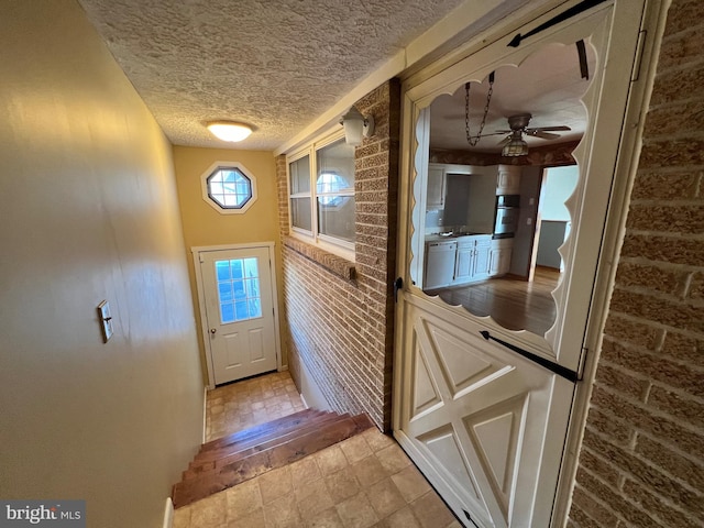 doorway to outside with brick wall, a textured ceiling, light tile flooring, and ceiling fan