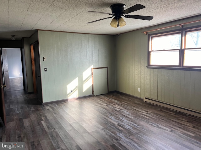 unfurnished room with ceiling fan, a baseboard heating unit, and dark hardwood / wood-style flooring