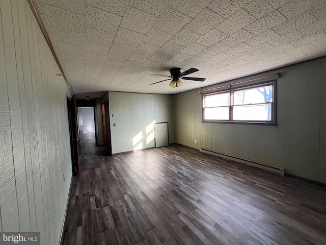 empty room featuring dark hardwood / wood-style flooring, ceiling fan, and a baseboard heating unit