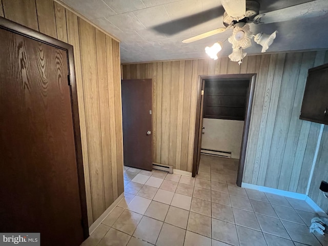 interior space with wood walls, light tile flooring, ceiling fan, and a baseboard heating unit