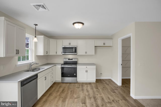 kitchen featuring white cabinetry, sink, hanging light fixtures, stainless steel appliances, and light hardwood / wood-style flooring