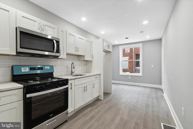 kitchen featuring appliances with stainless steel finishes, white cabinetry, light hardwood / wood-style floors, and sink