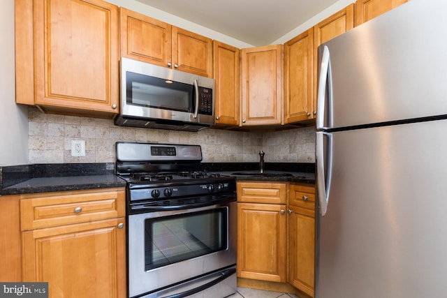 kitchen featuring sink, light tile floors, appliances with stainless steel finishes, dark stone countertops, and tasteful backsplash