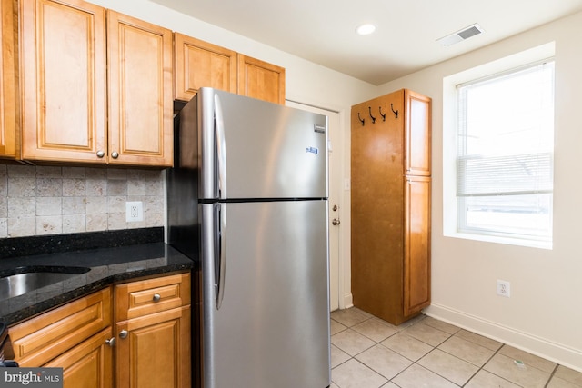 kitchen featuring dark stone counters, stainless steel refrigerator, a wealth of natural light, and light tile flooring