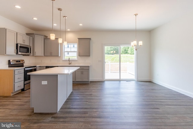 kitchen with appliances with stainless steel finishes, decorative light fixtures, gray cabinets, and a kitchen island