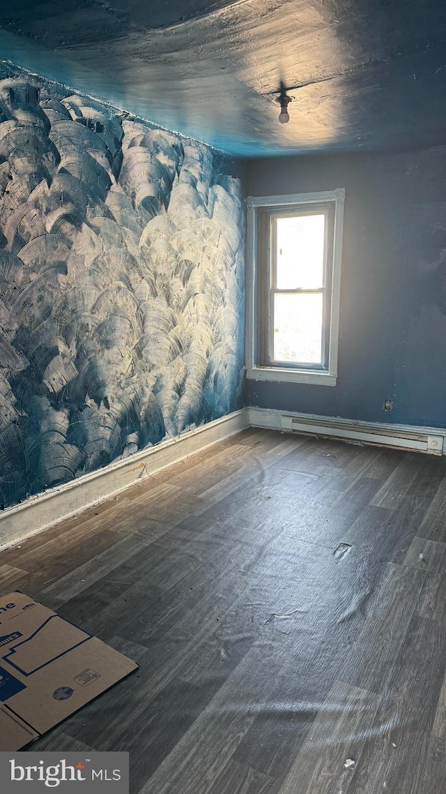 empty room featuring baseboard heating and dark hardwood / wood-style floors