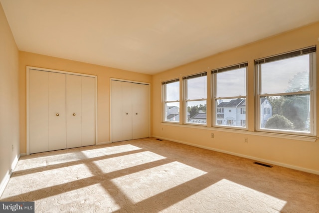 unfurnished bedroom featuring light colored carpet and multiple closets