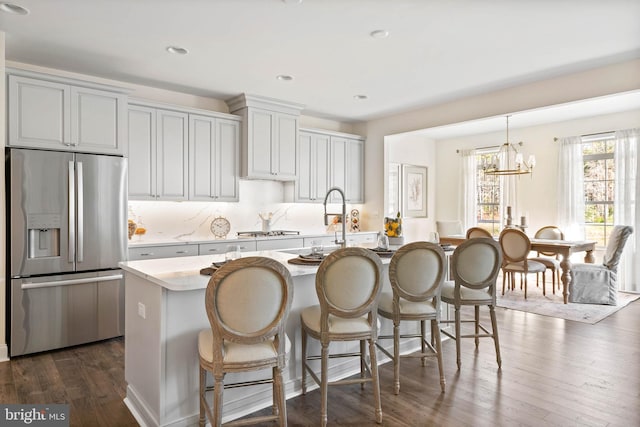 kitchen with a breakfast bar, appliances with stainless steel finishes, dark hardwood / wood-style floors, a notable chandelier, and a kitchen island with sink