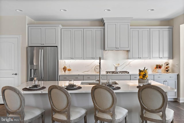 kitchen featuring a breakfast bar area, stainless steel fridge, backsplash, a kitchen island with sink, and dark hardwood / wood-style floors