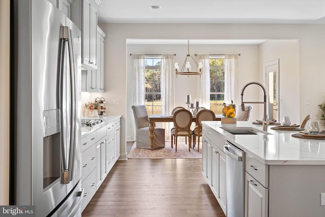 kitchen featuring decorative light fixtures, dark hardwood / wood-style floors, sink, stainless steel appliances, and a center island with sink