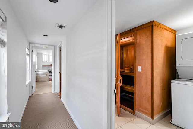 hallway featuring light colored carpet and stacked washer / drying machine