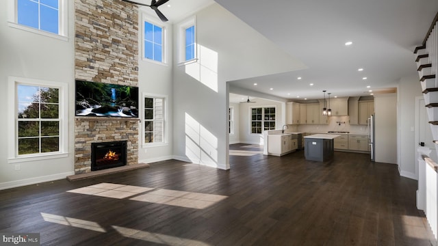 unfurnished living room featuring dark hardwood / wood-style flooring, a high ceiling, ceiling fan, and a stone fireplace