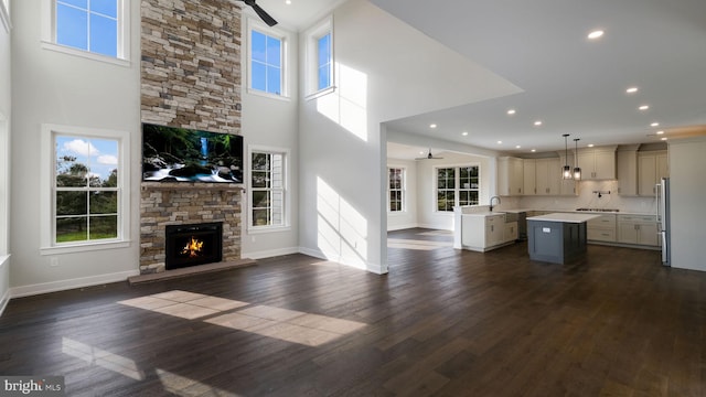 unfurnished living room featuring dark wood-type flooring, sink, a fireplace, a high ceiling, and ceiling fan