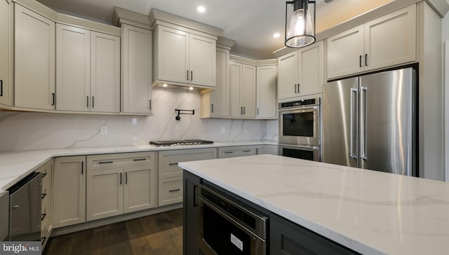 kitchen with pendant lighting, light stone counters, dark wood-type flooring, stainless steel appliances, and backsplash