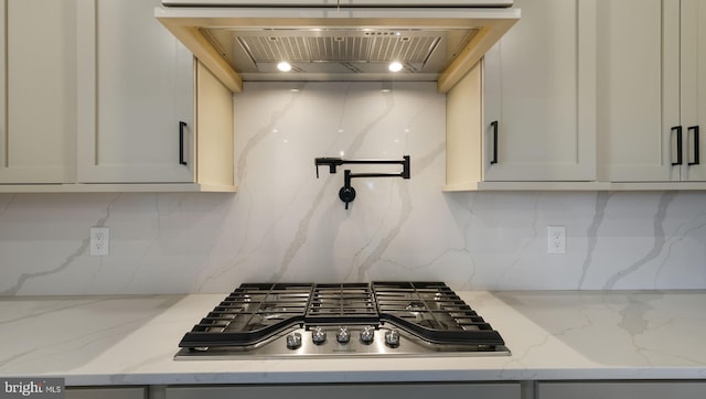 kitchen featuring light stone countertops, backsplash, wall chimney range hood, and stainless steel gas cooktop