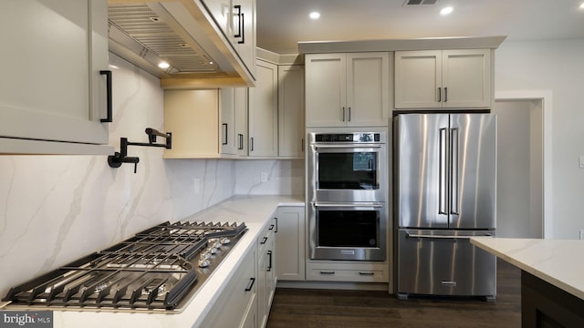 kitchen featuring appliances with stainless steel finishes, light stone counters, backsplash, dark hardwood / wood-style flooring, and exhaust hood