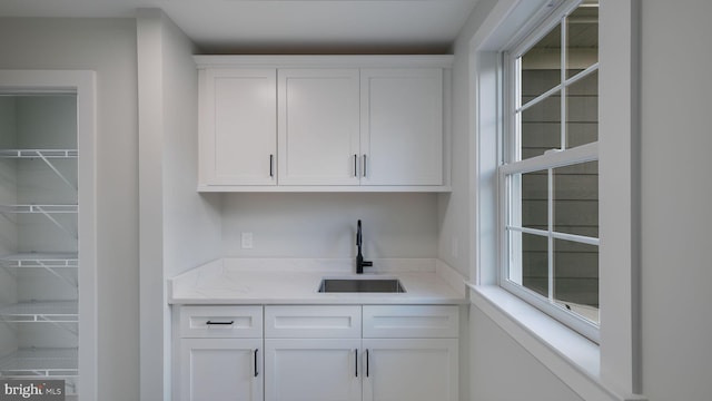 bar with light stone countertops, white cabinetry, and sink