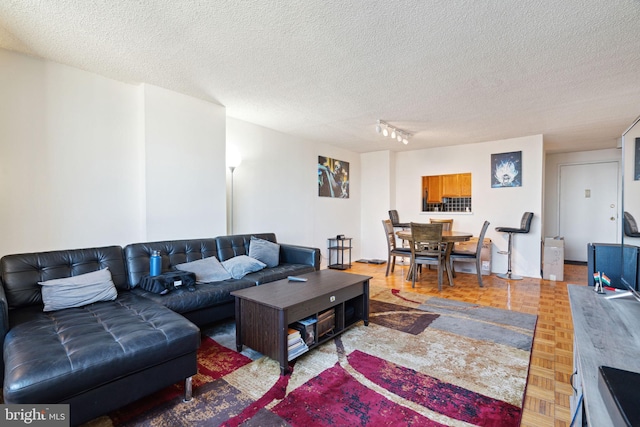 living room featuring parquet flooring, rail lighting, and a textured ceiling