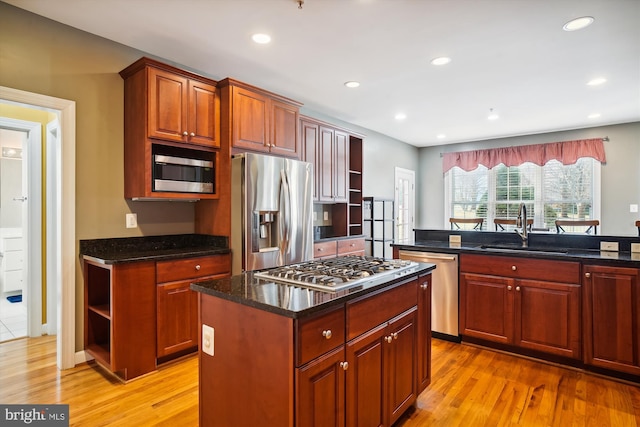 kitchen featuring stainless steel appliances, a center island, dark stone counters, light wood-type flooring, and sink