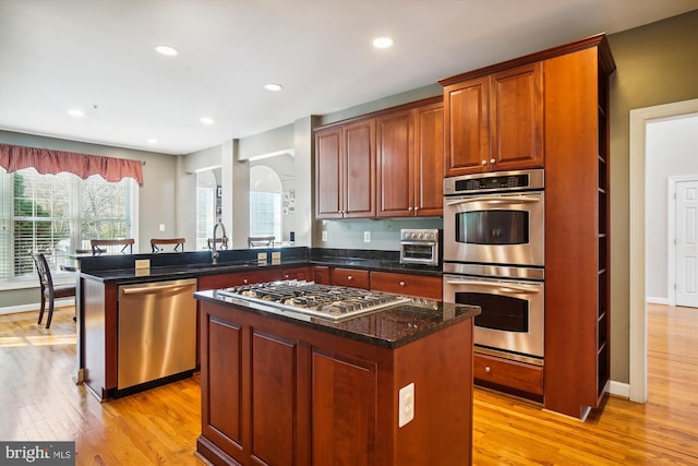 kitchen with dark stone counters, stainless steel appliances, a kitchen island, and light wood-type flooring