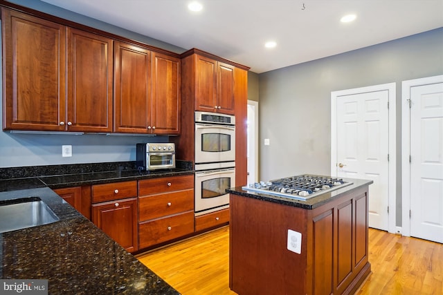 kitchen with stainless steel gas cooktop, double oven, light wood-type flooring, a center island, and dark stone counters