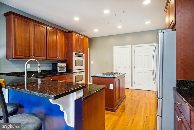 kitchen with light hardwood / wood-style floors, a center island, dark stone counters, a breakfast bar area, and appliances with stainless steel finishes