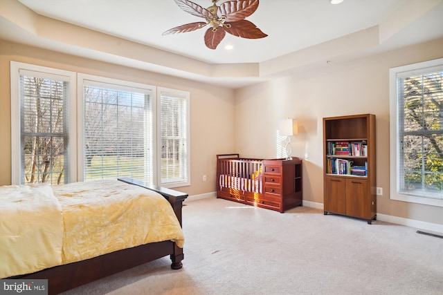 bedroom with light carpet, ceiling fan, and a raised ceiling