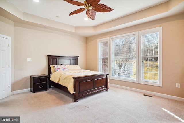 bedroom featuring a raised ceiling, light colored carpet, ceiling fan, and multiple windows