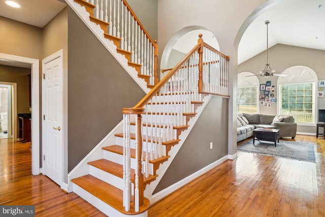 stairs with a high ceiling, ceiling fan, and light hardwood / wood-style flooring