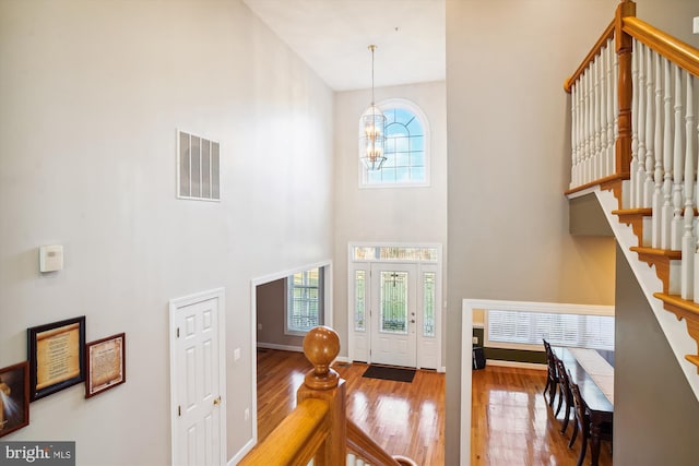 entryway with a notable chandelier, hardwood / wood-style floors, and a towering ceiling