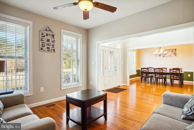 living room featuring light wood-type flooring, a wealth of natural light, and ceiling fan with notable chandelier