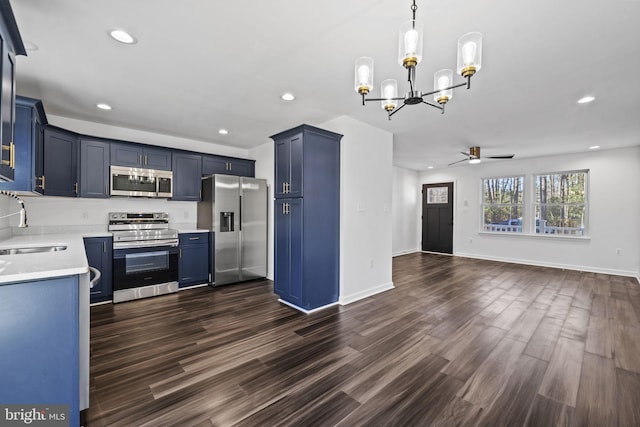 kitchen with appliances with stainless steel finishes, hanging light fixtures, dark wood-type flooring, blue cabinetry, and ceiling fan with notable chandelier