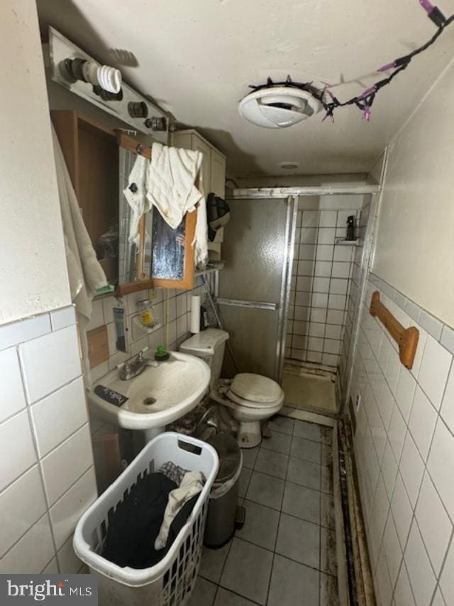 bathroom featuring tile patterned flooring, a shower with door, sink, and tile walls