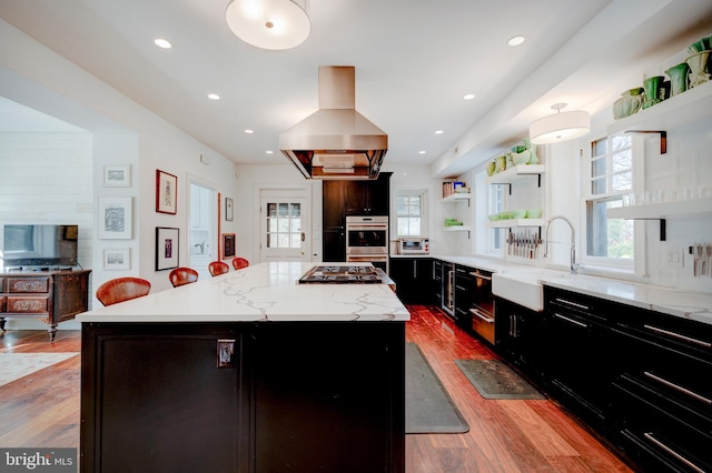 kitchen featuring appliances with stainless steel finishes, a kitchen island, sink, and wall chimney range hood