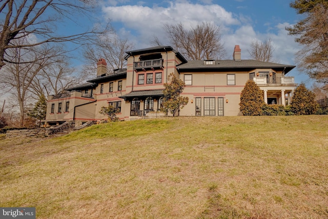 back of house featuring a balcony, french doors, and a lawn