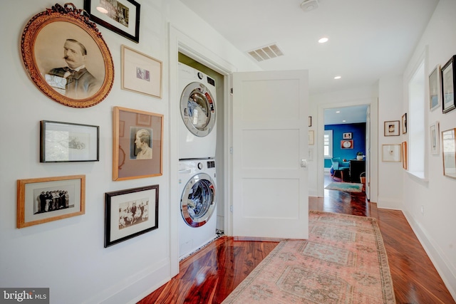 laundry area featuring stacked washer and clothes dryer and dark hardwood / wood-style flooring