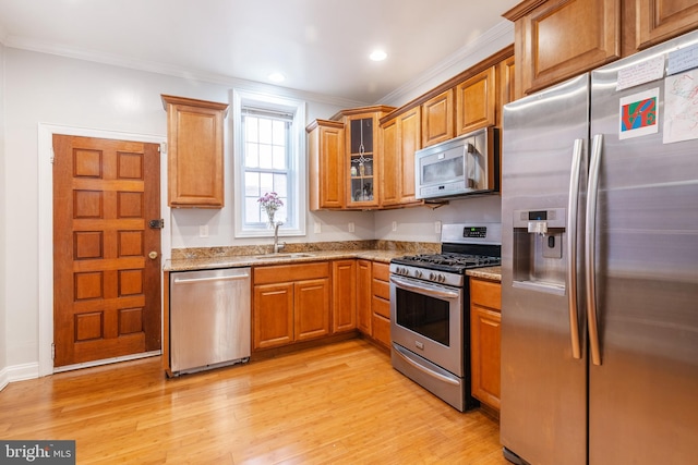 kitchen with sink, light stone counters, ornamental molding, appliances with stainless steel finishes, and light wood-type flooring