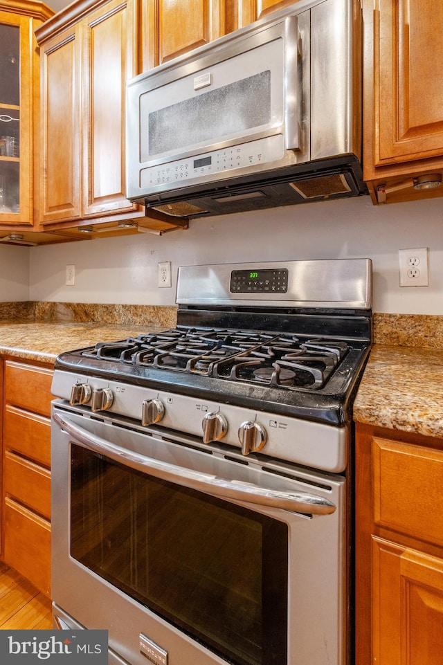 kitchen with stainless steel gas range oven, light stone counters, and light hardwood / wood-style flooring