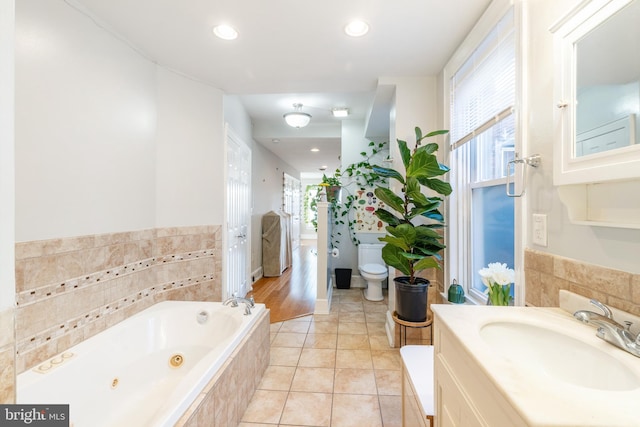 bathroom featuring toilet, vanity, a relaxing tiled bath, and tile flooring