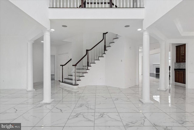 entryway with light tile floors, ornate columns, a high ceiling, and ornamental molding