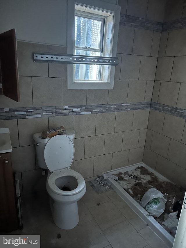 bathroom with tile walls, toilet, vanity, and tile flooring