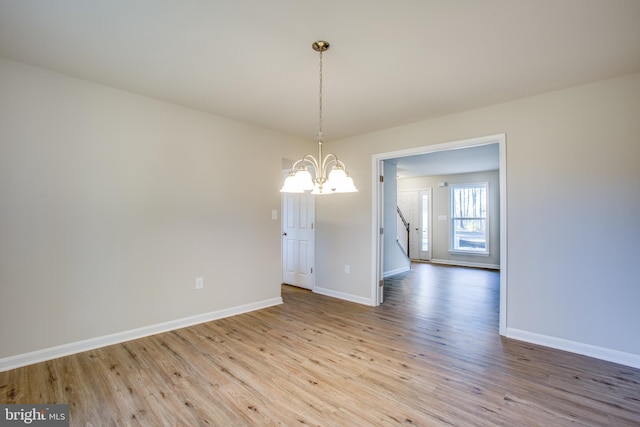 empty room featuring a notable chandelier and light hardwood / wood-style floors