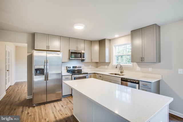 kitchen with gray cabinetry, appliances with stainless steel finishes, sink, light wood-type flooring, and a kitchen island