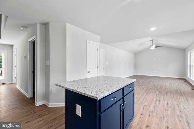 kitchen featuring lofted ceiling, ceiling fan, light wood-type flooring, light stone counters, and a kitchen island